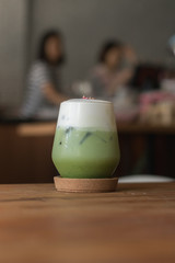 Green Tea with milk foam. served in beautiful glass. indoor cafe.Barista background.