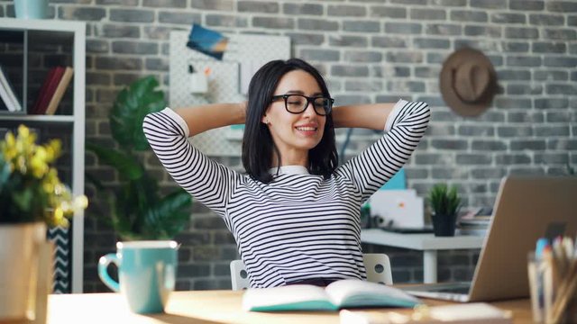 Seamless loop of happy young lady smiling looking at laptop screen in office sitting at desk with raised arms. Successful work and cheerful youth concept.