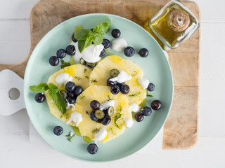 vista de arriba rodajas de piña fresca con arándanos yogurt y hojas de menta en plato verde sobre tabla de madera 