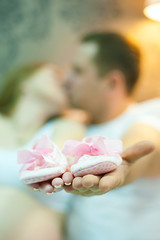 Obraz na płótnie Canvas поцелуй, беременность, пара, мама и папа, держут в руках детские тапочки, обувь для новорожденного, розовая детская обувь.jpg