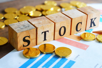 Text "STOCK" on wood cube with gold coins on chart document, economic data concept.