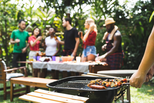 Young boy cooking meat on barbecue grill for Group of friends at summer outdoor party and holidays concept..