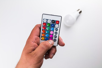Blurred led light bulb and remote in foreground held by male hand on white background
