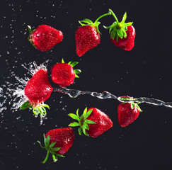 Bright and juicy strawberries thrown into the air on a black and gray background with chaotic splashes of water