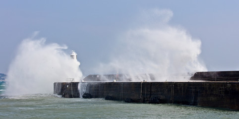 Fototapeta na wymiar Waves breaking over Penzance's harbour wall and lighthouse, Cornwall, England, UK.