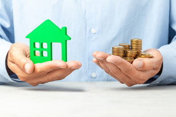 Man in blue shirt is holding a house and stack of coins. The concept of buying house, real estate...