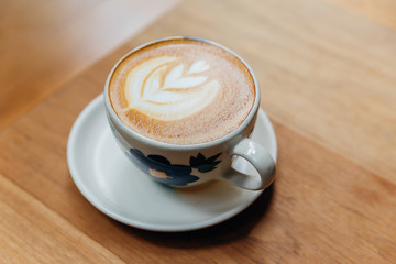 Latte art heart shape served in ceramic cup on wooden table.