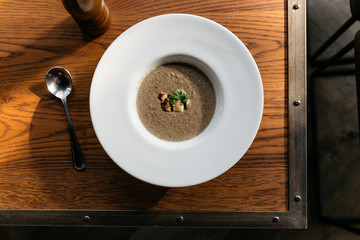 Top view of mushroom soup with Grouton in white plate with sunlight on wooden table.