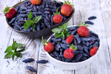 Fresh honeysuckles and strawberries in bowls topped with mint on white table