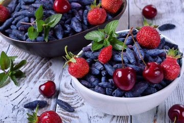 Honeysuckles, strawberries and cherries in white bowl on the table. Freshly picked berries