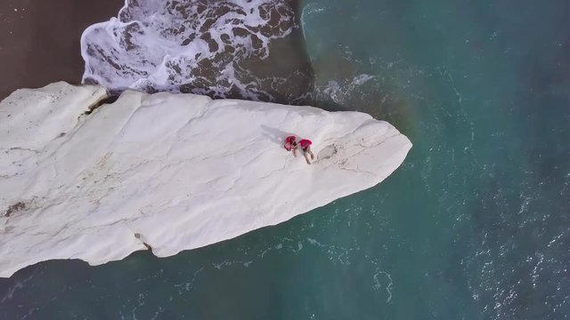 aerial view of family on white stone cape in Kalymnos or Governor Beach in Cyprus, father mother and son in red shirt sits on sea coast, traveling and vacation, shooting vertically from above