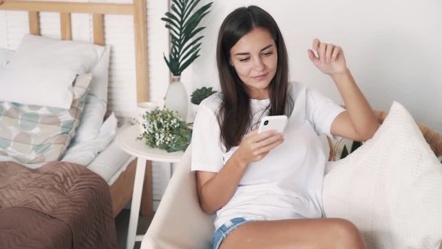 Beautiful girl sits in straw chair and uses phone for shopping online, slow motion