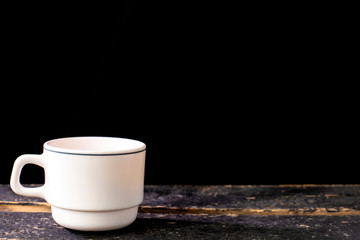 Obraz na płótnie Canvas White coffee mug on wooden table and black background with space for text. Composition for coffee shop and coffee making