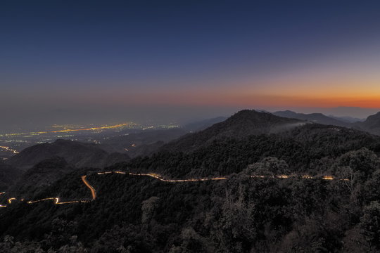 sunset at Doi Ang Khang, view evening of light trails on the road along side hill with mountain and twilight sky background, Monzone Camping Zone, Doi Angkhang, Chiang Mai, Thailand.