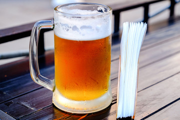 A mug of cold beer, misted droplets roll down the glass. On the table next to the napkin holder with napkins.