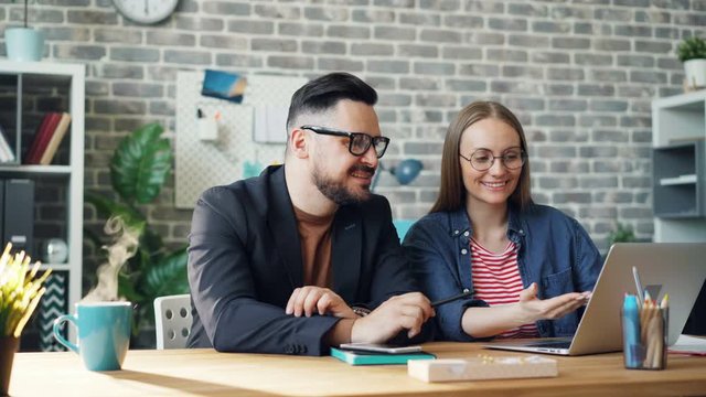 Cinemagraph loop of happy coworkers girl and guy using laptop while steam going up from hot drink tasty coffee in office. People, colleagues and work concept.