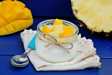 Glass jar with yogurt and pineapple cubes with mango on a wooden table