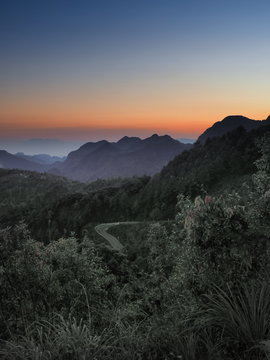 View evening of the road on side hill and Doi Luang Chiang Dao Peak Mountain with yellow sun light in the sky background, taken from Monzone View Point, Doi Ang Khang, Chiang Mai, Thailand.
