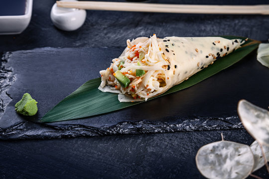 Close-up of tasty hand roll sushi in mamenori with crab and Tobico caviar served on dark stone plate with soy sauce and ginger. Copy space. Temaki, Japanese cuisine. Healthy food