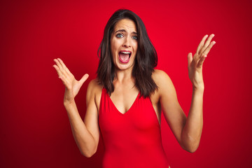 Beautiful woman wearing bikini swimwear over red isolated background celebrating crazy and amazed for success with arms raised and open eyes screaming excited. Winner concept