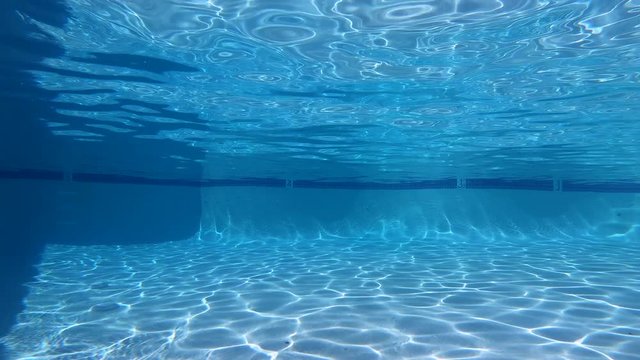 Empty underwater swimming pool with moving sunlight patterns.