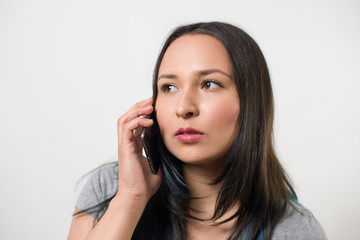 thoughtful young girl talking on the phone and looking away. On light background
