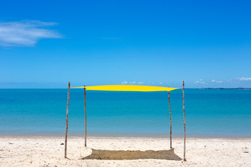 Beautiful beach view with a yellow tent on sunny summer day and sea and blue sky in the background. Concept of vacations, peace and relaxation. Ponta do Corumbau, Bahia, Brazil.