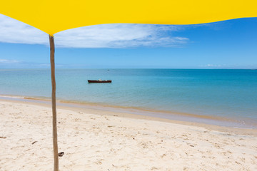 Beautiful beach view with a yellow tent on sunny summer day and sea and blue sky in the background. Concept of vacations, peace and relaxation. Ponta do Corumbau, Bahia, Brazil.