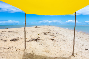 Beautiful beach view with a yellow tent on sunny summer day and sea and blue sky in the background. Concept of vacations, peace and relaxation. Ponta do Corumbau, Bahia, Brazil.