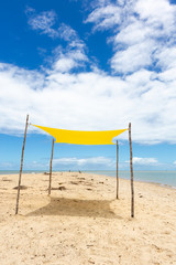 Beautiful beach view with a yellow tent on sunny summer day and sea and blue sky in the background. Concept of vacations, peace and relaxation. Ponta do Corumbau, Bahia, Brazil.