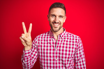 Young handsome man over red isolated background smiling looking to the camera showing fingers doing victory sign. Number two.