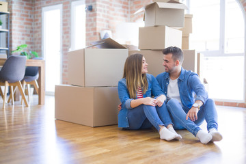 Fototapeta na wymiar Young beautiful couple in love moving to new home, sitting on the floor very happy and cheerful for new apartment around cardboard boxes
