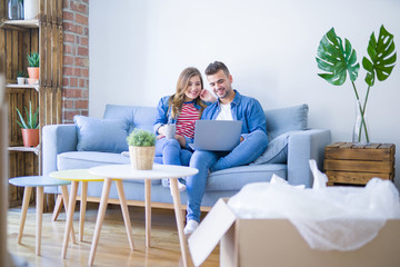 Young couple relaxing sitting on the sofa using the computer laptop around cardboard boxes, very happy moving to a new house