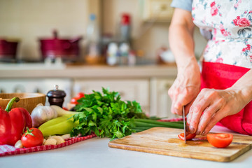 Female hand with knife chops tomato in kitchen. Cooking vegetables