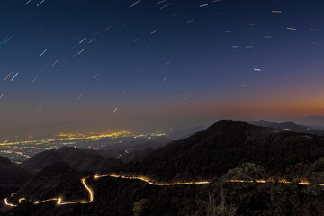 Mountain view at night of Light Trails on the road with mountain and Star Trails in dark sky background, Monzone view point, Doi Ang Khang, Chiang Mai, Thailand. 