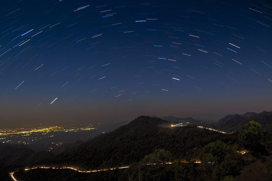 Mountain view at night of Light Trails on the road with mountain and Star Trails in dark sky background, Monzone view point, Doi Ang Khang, Chiang Mai, Thailand. 