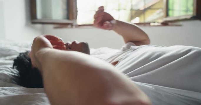 Slow motion of young handsome man is relaxing in the bedroom in the early morning in a sunny day.
