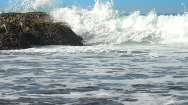 huge ocean waves crush into brown rock foaming under clear blue summer sky slow motion. Concept low tide and ecosystem change