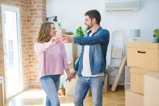 Young couple dancing celebrating moving to new apartment around cardboard boxes