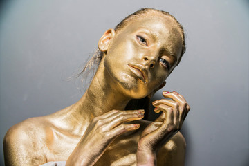 Fashion model woman golden skin face in bright sparkles, Trendy glowing gold skin make-up. Glitter...