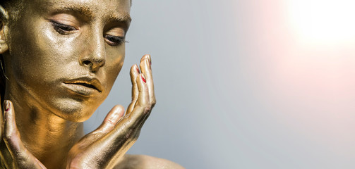 Fashion model woman golden skin face in bright sparkles, Trendy glowing gold skin make-up. Glitter metallic shine   makeup 