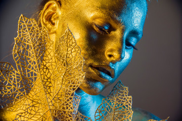Fashion model woman golden skin face in bright sparkles, Trendy glowing gold skin make-up. Glitter metallic shine   makeup 