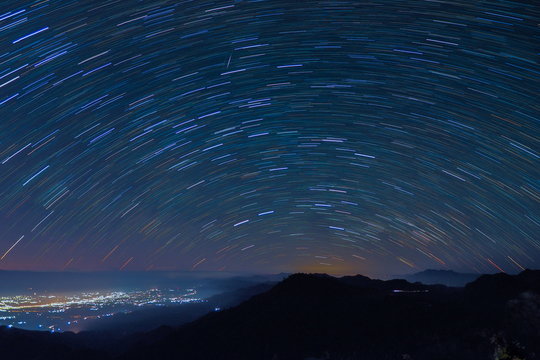 Time-Lapse Mountain view at night of peak mountain with city ligh and Star Trails in dark sky background, Monzone view point, Doi Ang Khang, Chiang Mai, Thailand. 