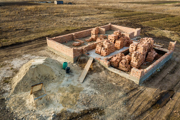 Aerial view of building site. Trenches dug in ground and filled with cement as foundation for future house, brick basement floor and stacks of brick for construction.