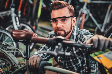 Happy attractive man in protective glasses and shirt is checkin bicycles chain for customer.
