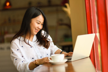 Asian woman using  laptop working and drink coffee in cafe