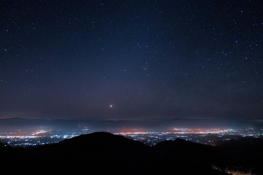Mountain view morning at night of top hills and city around with soft fog under the stars in dark sky background, Monzone View Point Doi Ang Khang, Chiang Mai, northern of Thailand.