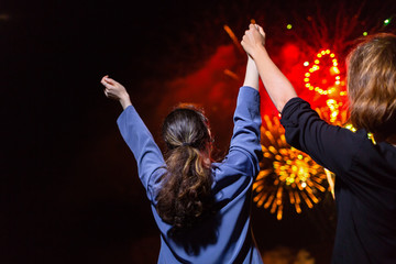 Two young women enjoy the fireworks in the sky at the festival. Concept of festivals and holidays. The view from the back
