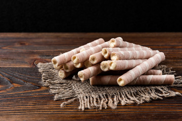 Sweet chocolate waffle rolls on dark wooden background.