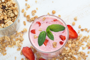 A glass of healthy strawberry yogurt with fresh berries, muesli and mint on a white wooden table. Healthy breakfast.